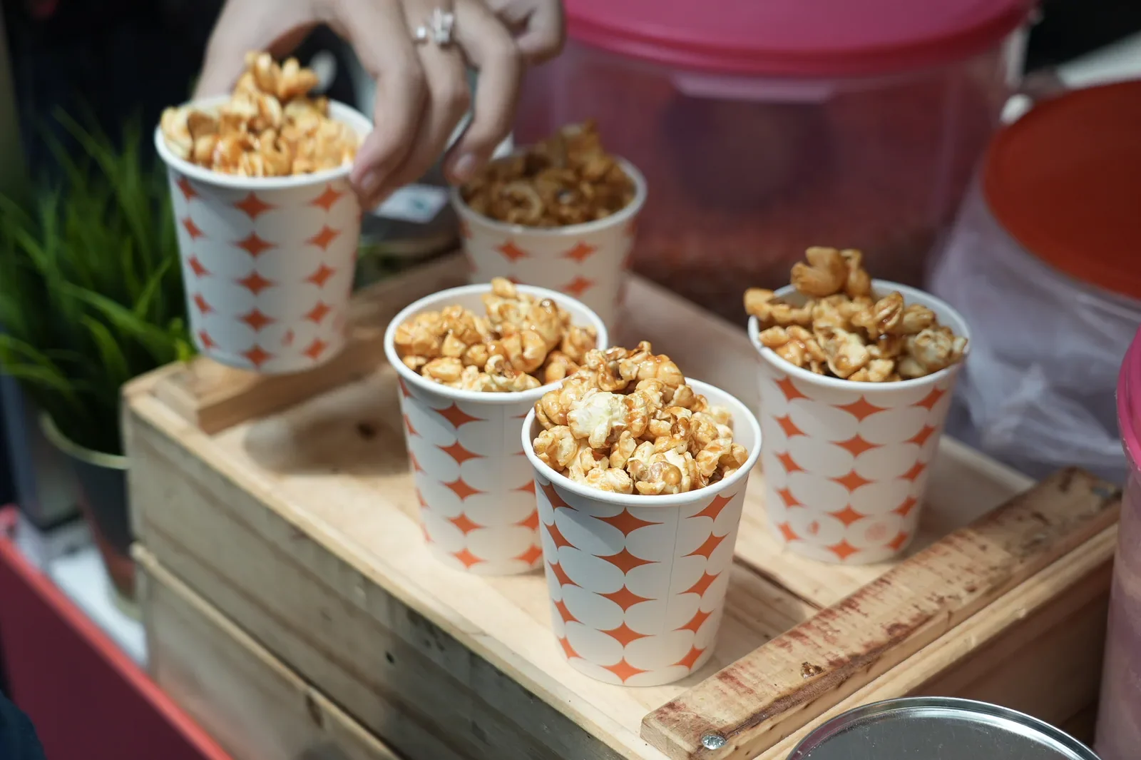 Paper cups filled with popcorn arranged on a wooden serving tray