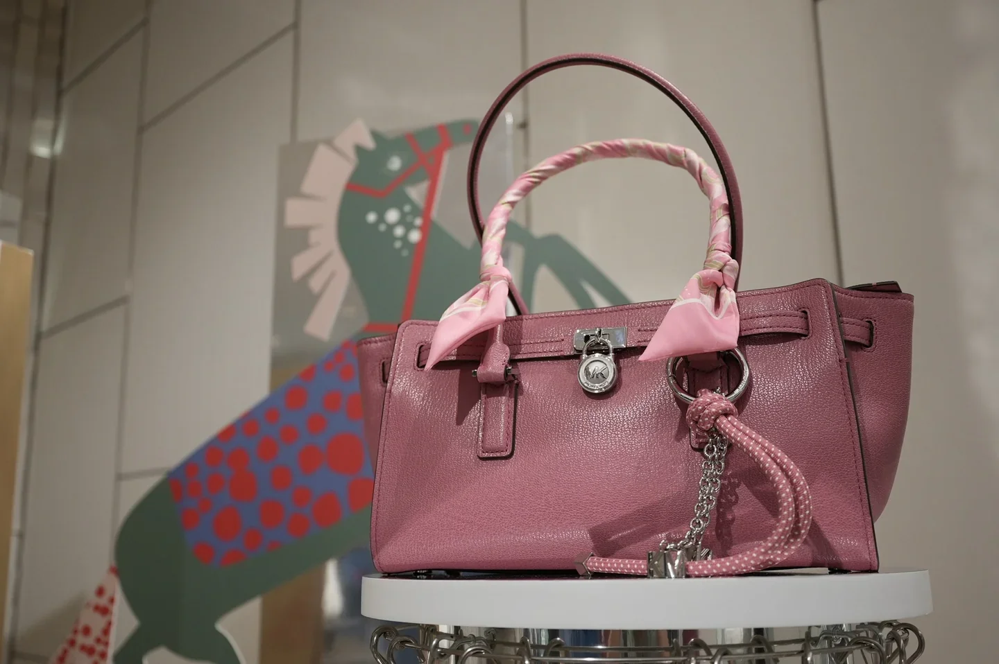 A pink Michael Kors handbag displayed against illustrated seasonal graphics.