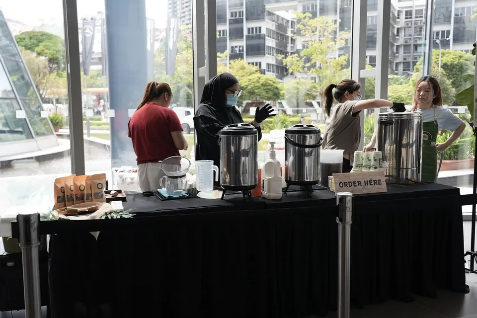 Event staff preparing drinks and service equipment on a table beside showroom windows