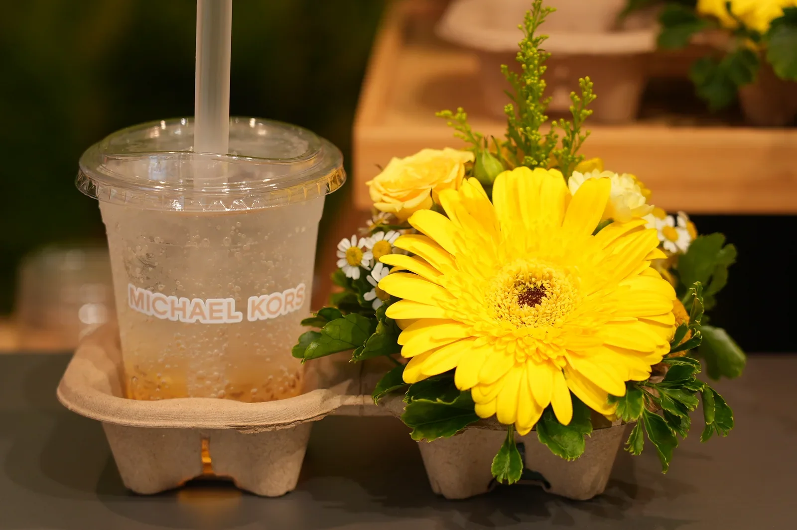 A Michael Kors branded drink and yellow flower arrangement in a paired takeaway holder