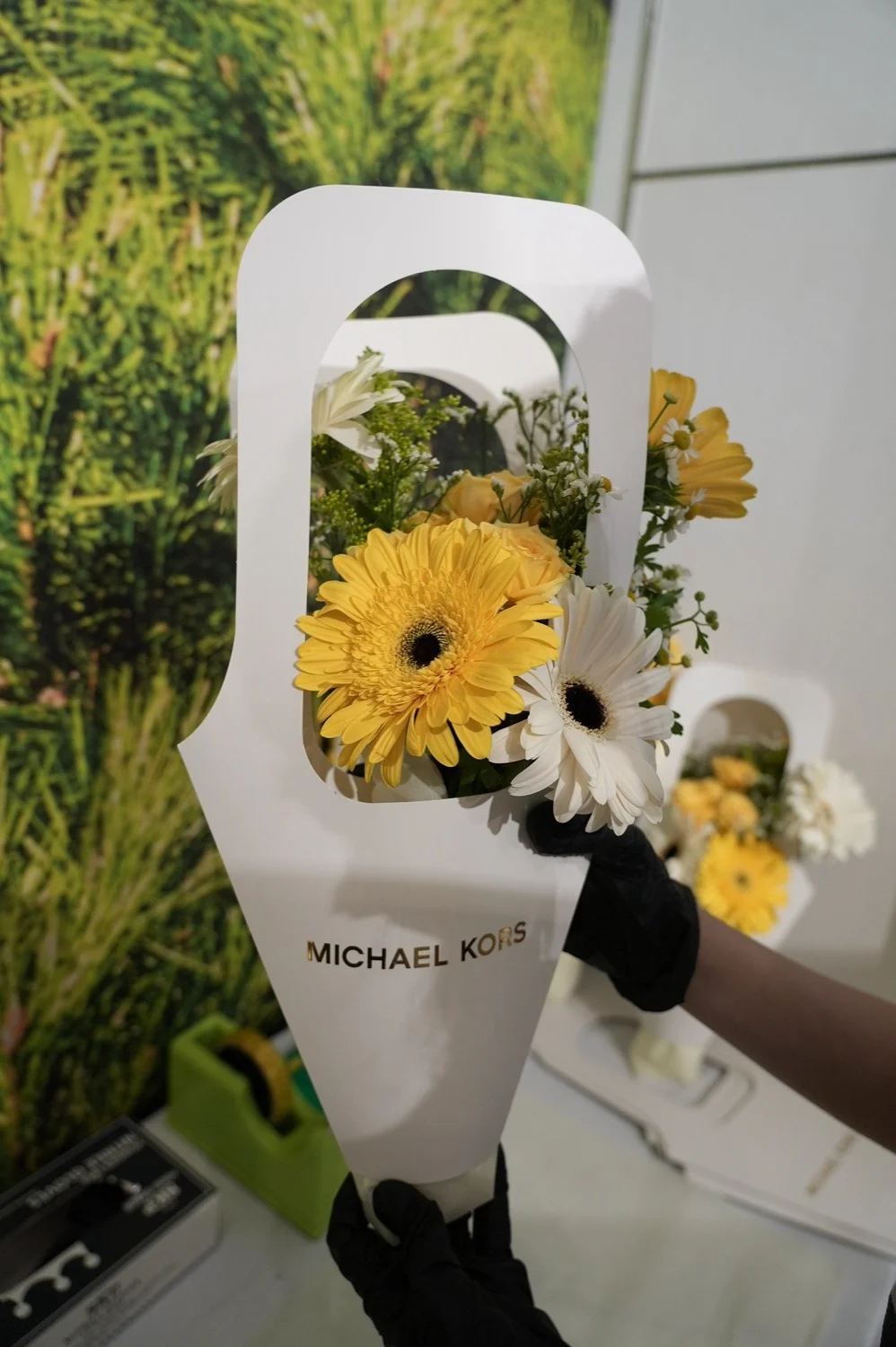 A finished yellow and white floral arrangement in a Michael Kors branded carrier